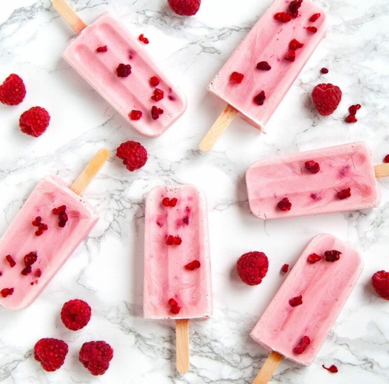 Six raspberry popsicles with wooden popsicle sticks lying uneaten on a marble countertop