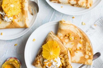 Breakfast crepes and oranges on white plate on marble kitchen counter