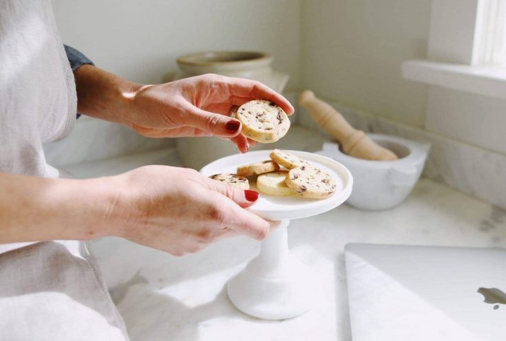 Small shortbread cookies on a cake stand. Woman's hands holding the cake stand and one cookie