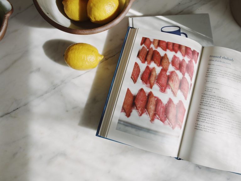 Lemons in a bowl and a cookbook open to a recipe photographed on a marble kitchen counter