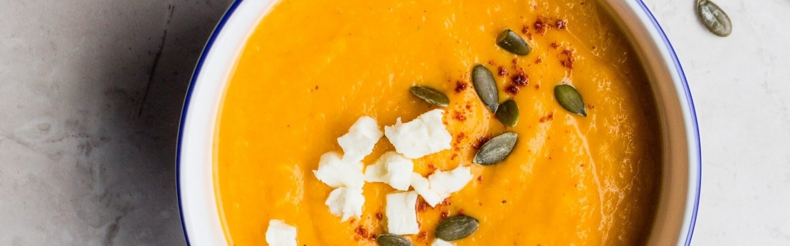 A bowl of orange carrot soup on a kitchen counter