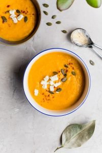 A bowl of orange carrot soup on a kitchen counter