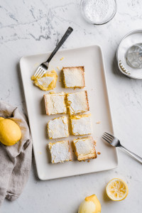 Organic and gluten free lemon bars ready-to-serve and one already nibbled on, placed on a marble counter top