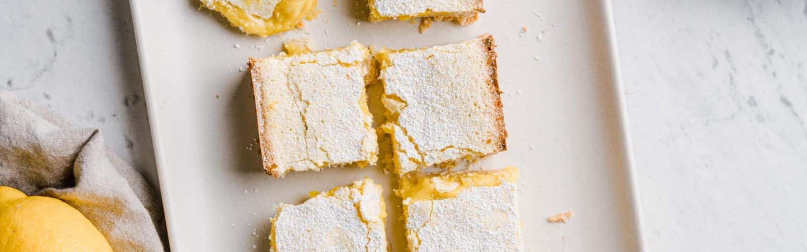 Organic and gluten free lemon bars ready-to-serve and one already nibbled on, placed on a marble counter top